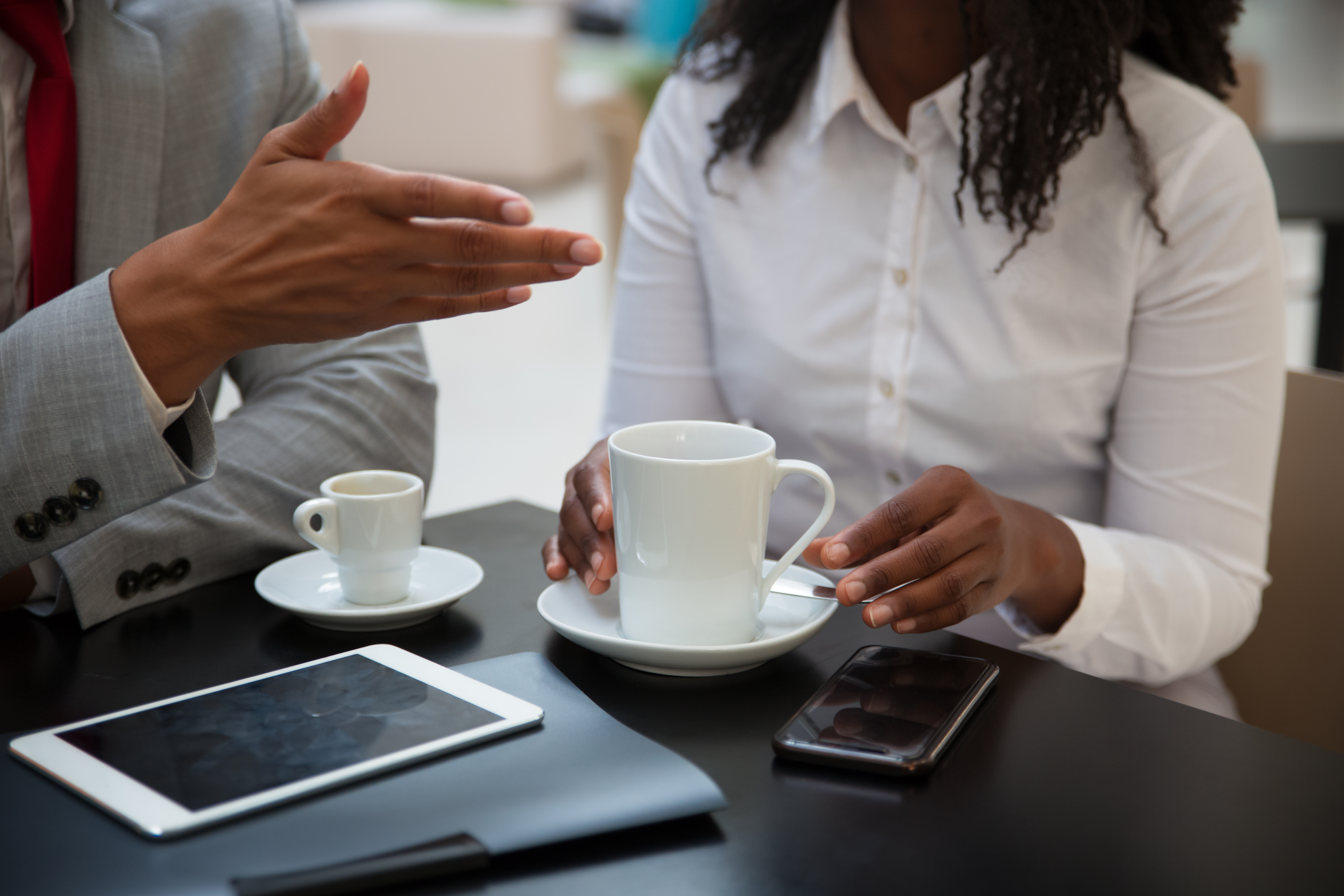 Closeup of business colleagues discussing work issues in coffee shop. Hands of business people sitting at table with cups and digital devices, drinking coffee, gesturing. Business talk concept